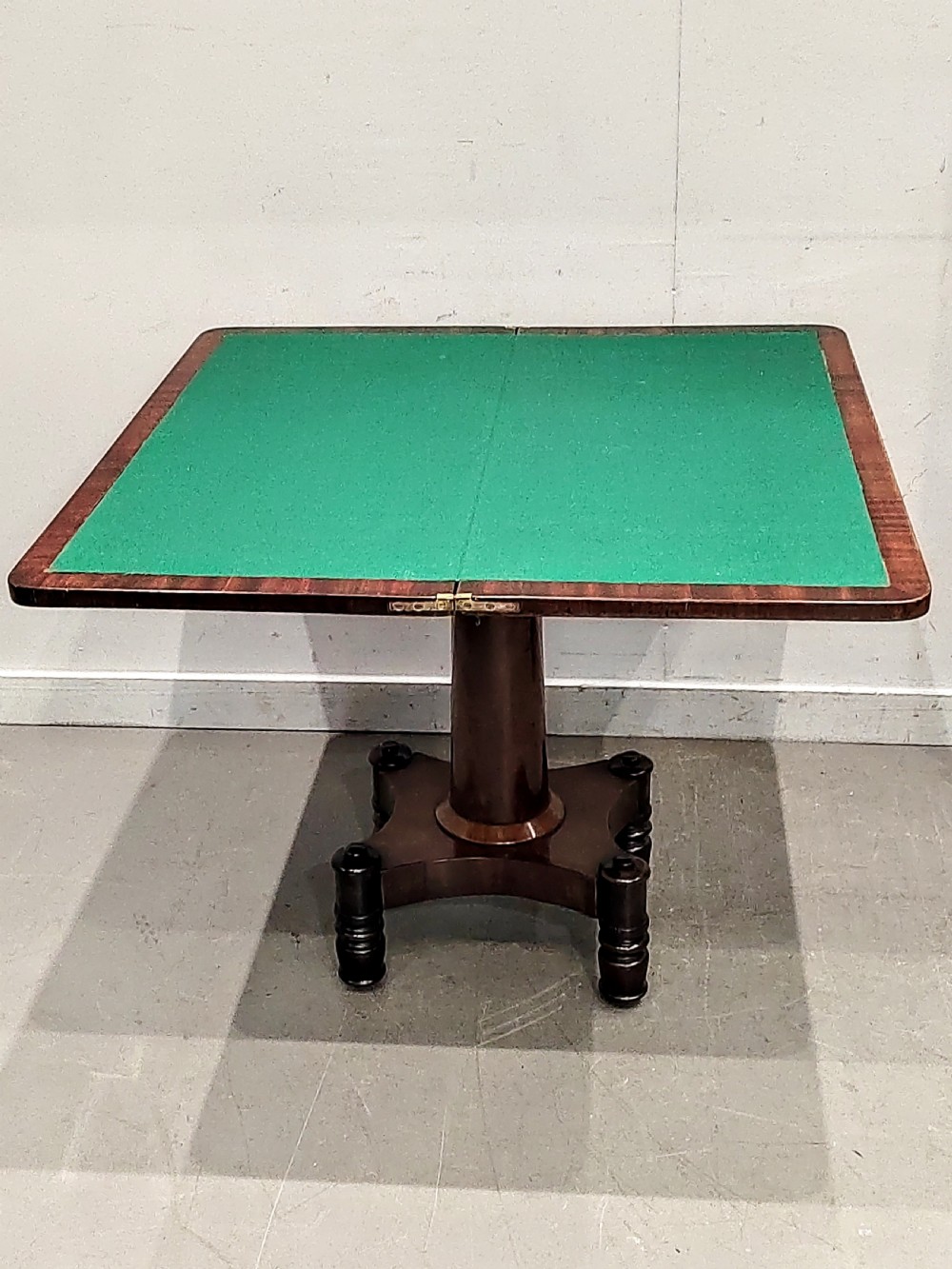 A Georgian mahogany card table featuring a hinged fold-over top, carved acanthus apron brackets, a turned pedestal column, and a shaped plinth base on turned feet. View II