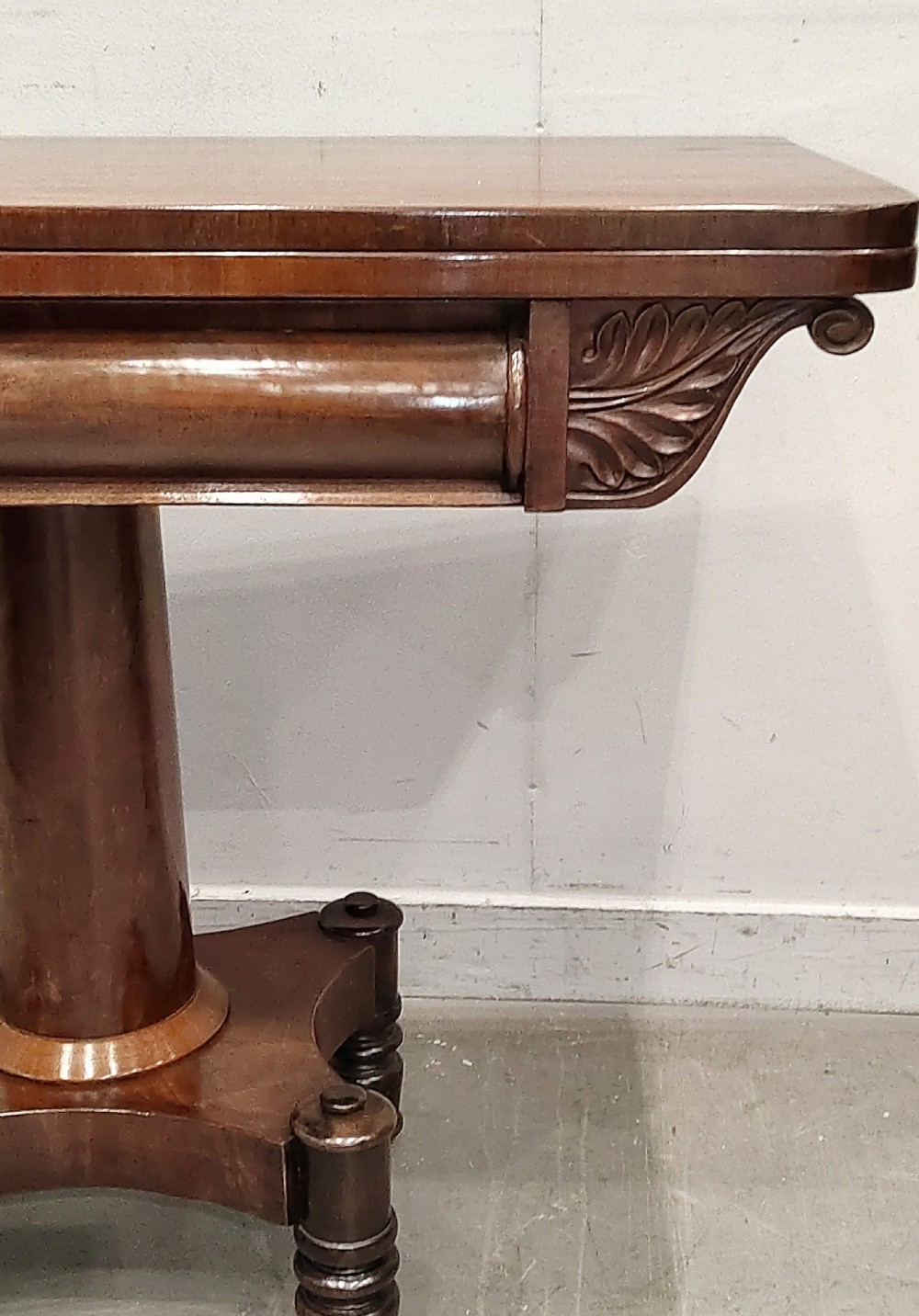 A Georgian mahogany card table featuring a hinged fold-over top, carved acanthus apron brackets, a turned pedestal column, and a shaped plinth base on turned feet. View V