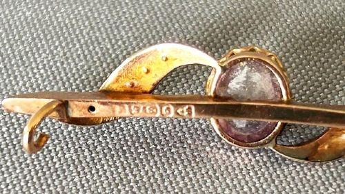 An Edwardian 9ct yellow gold bar brooch featuring a central claw-set oval amethyst flanked by S-scroll shoulders set with tiny seed pearls. View V