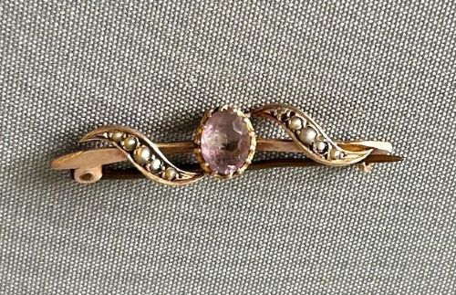 An Edwardian 9ct yellow gold bar brooch featuring a central claw-set oval amethyst flanked by S-scroll shoulders set with tiny seed pearls. View VI