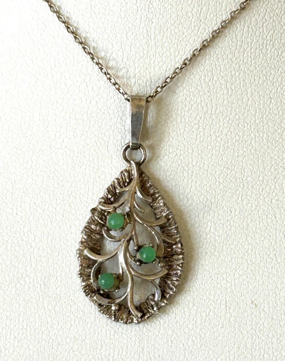 A teardrop-shaped silver pendant featuring textured edges, openwork branch motifs, and three small green chrysoprase cabochons suspended on a fine silver chain.