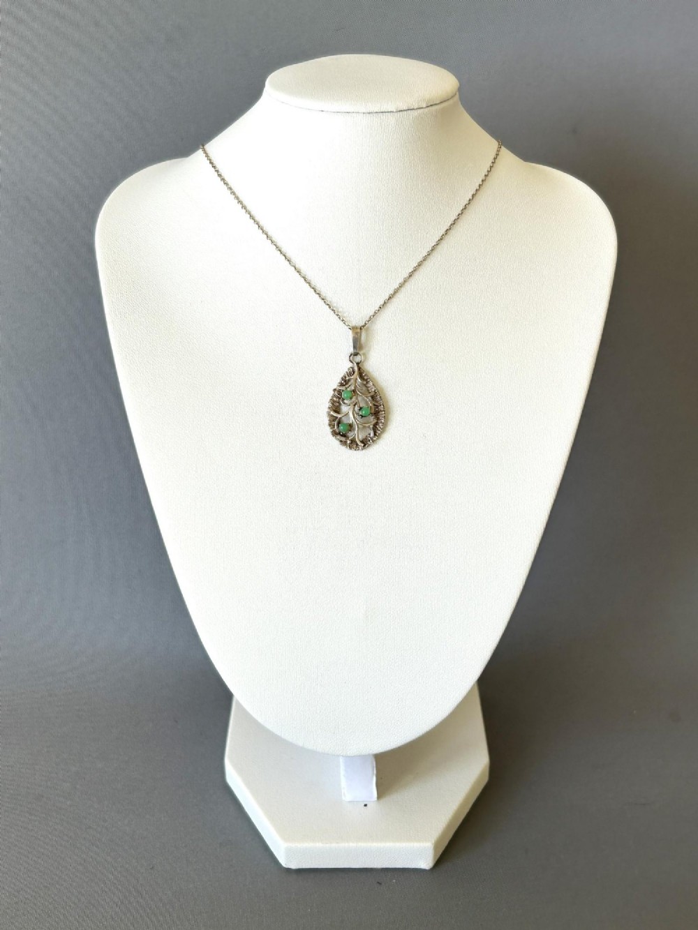 A teardrop-shaped silver pendant featuring textured edges, openwork branch motifs, and three small green chrysoprase cabochons suspended on a fine silver chain. View III