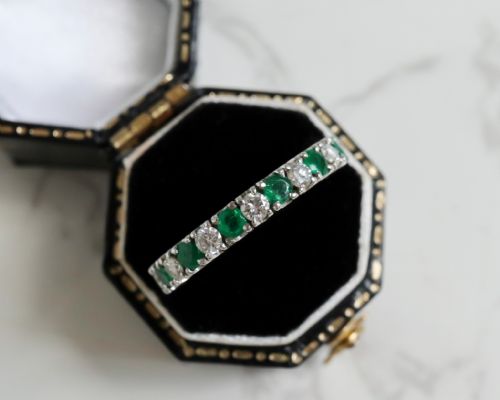 fig 1. An antique platinum full eternity ring set with alternating round green emeralds and white diamonds in a claw setting.