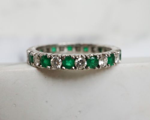 fig 4. An antique platinum full eternity ring set with alternating round green emeralds and white diamonds in a claw setting.