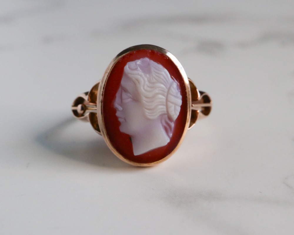 An antique nine-carat gold ring featuring an oval relief carving of a classical female profile set against a red background.