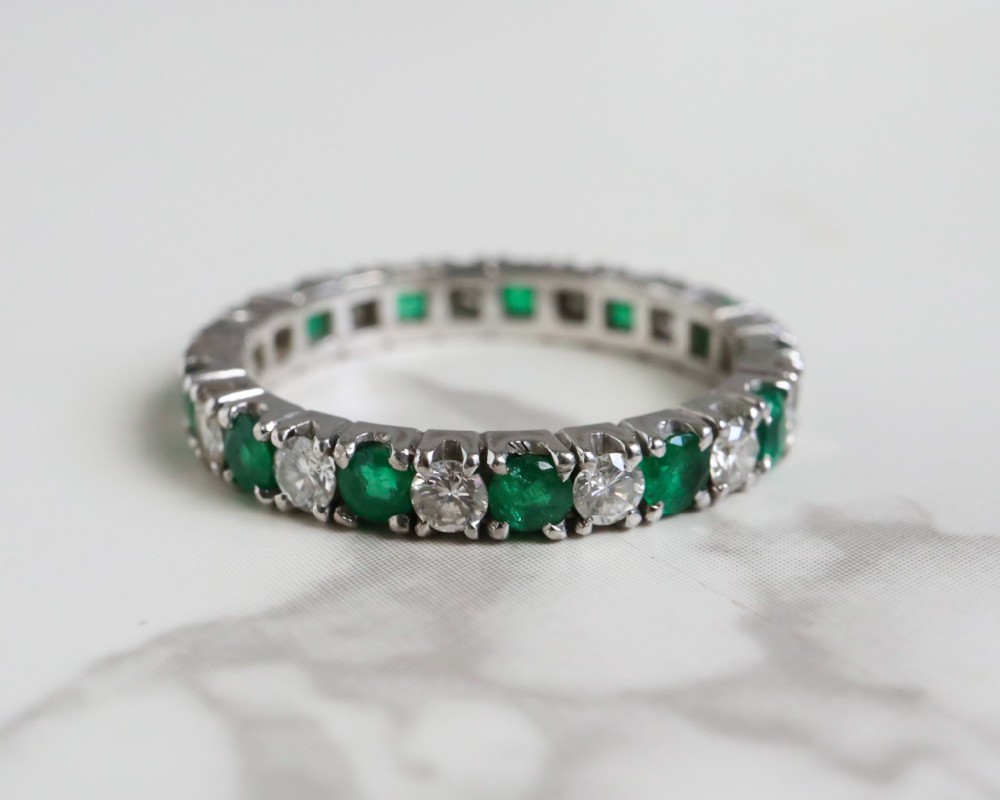 An antique platinum full eternity ring set with alternating round green emeralds and white diamonds in a claw setting.