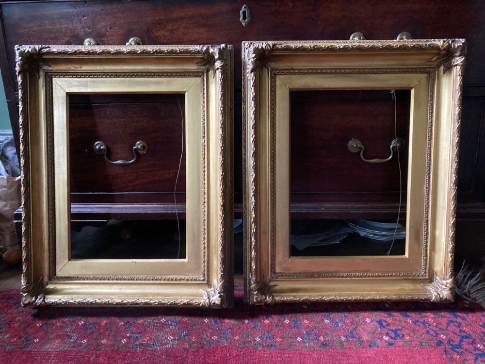 A matching pair of rectangular antique gilt gesso picture frames featuring ornate corner carvings and leaf motif mouldings.
