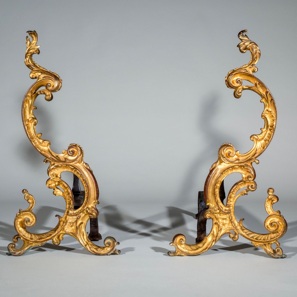 A pair of 18th-century gilt bronze Rococo andirons featuring swept C-scrolls, acanthus leaf carving, and iron rear billet bars.