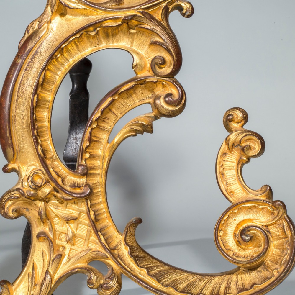 A pair of 18th-century gilt bronze Rococo andirons featuring swept C-scrolls, acanthus leaf carving, and iron rear billet bars. View V