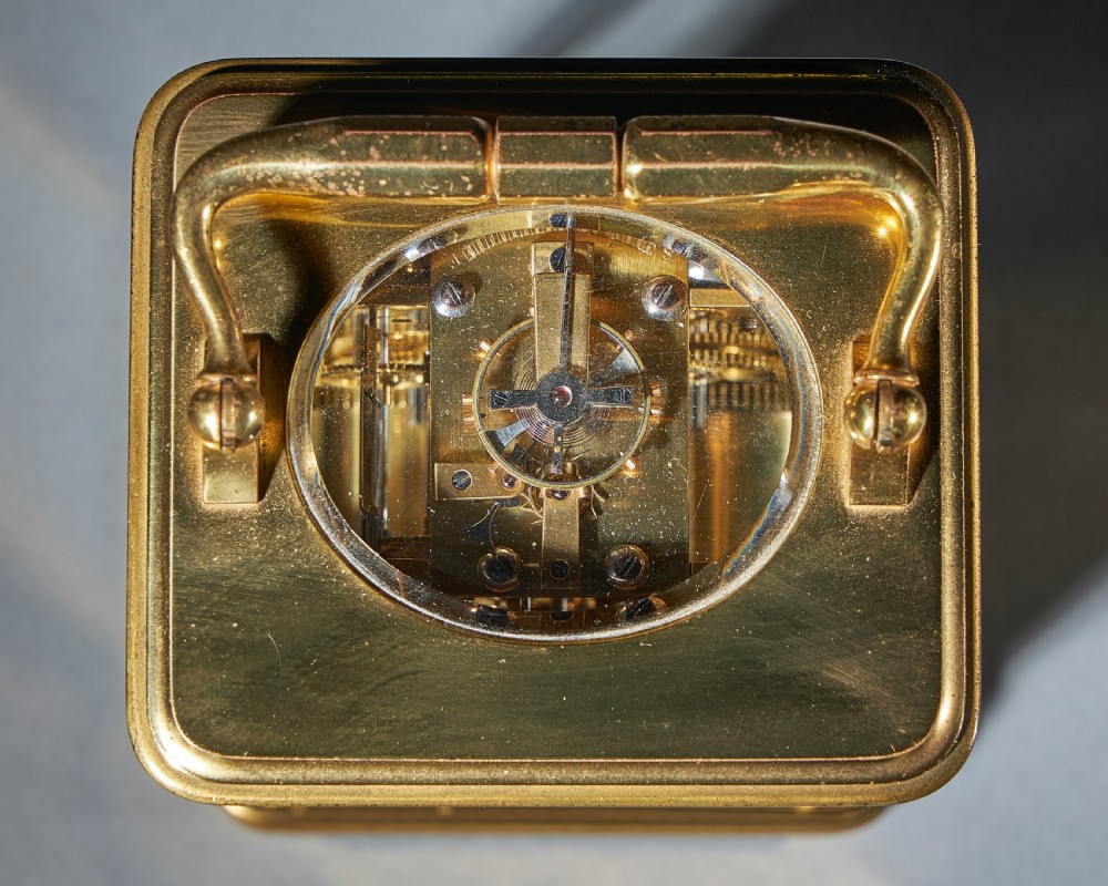A 19th-century gilt-brass carriage clock featuring a rectangular corniche case, a top folding handle, an engraved foliage face mask, and a white circular dial with Roman numerals. View VIII