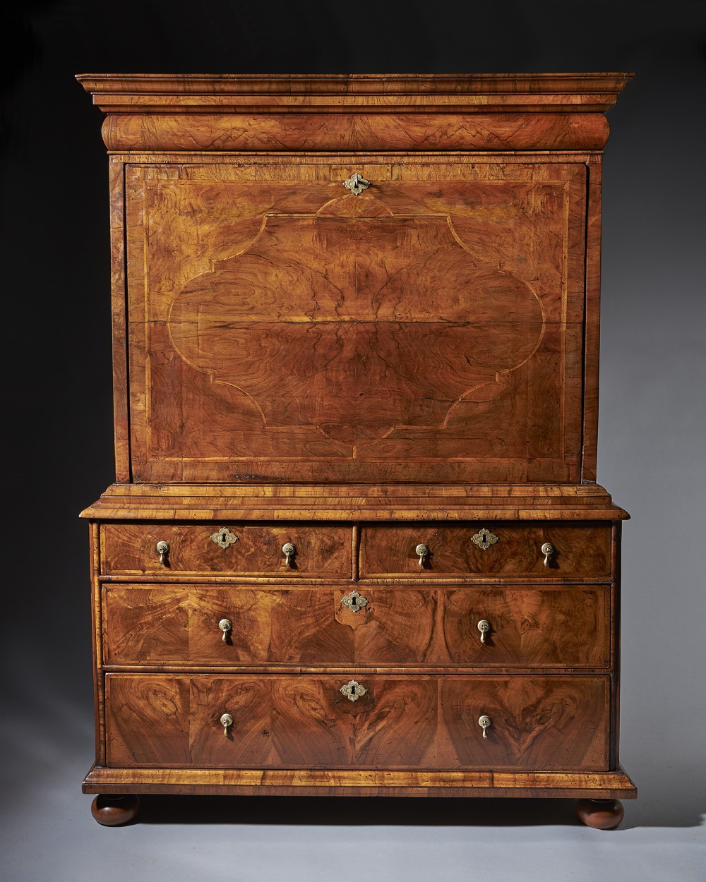 A late 17th-century William and Mary figured walnut escritoire featuring a fall-front desk section above a chest of drawers with turned bun feet.