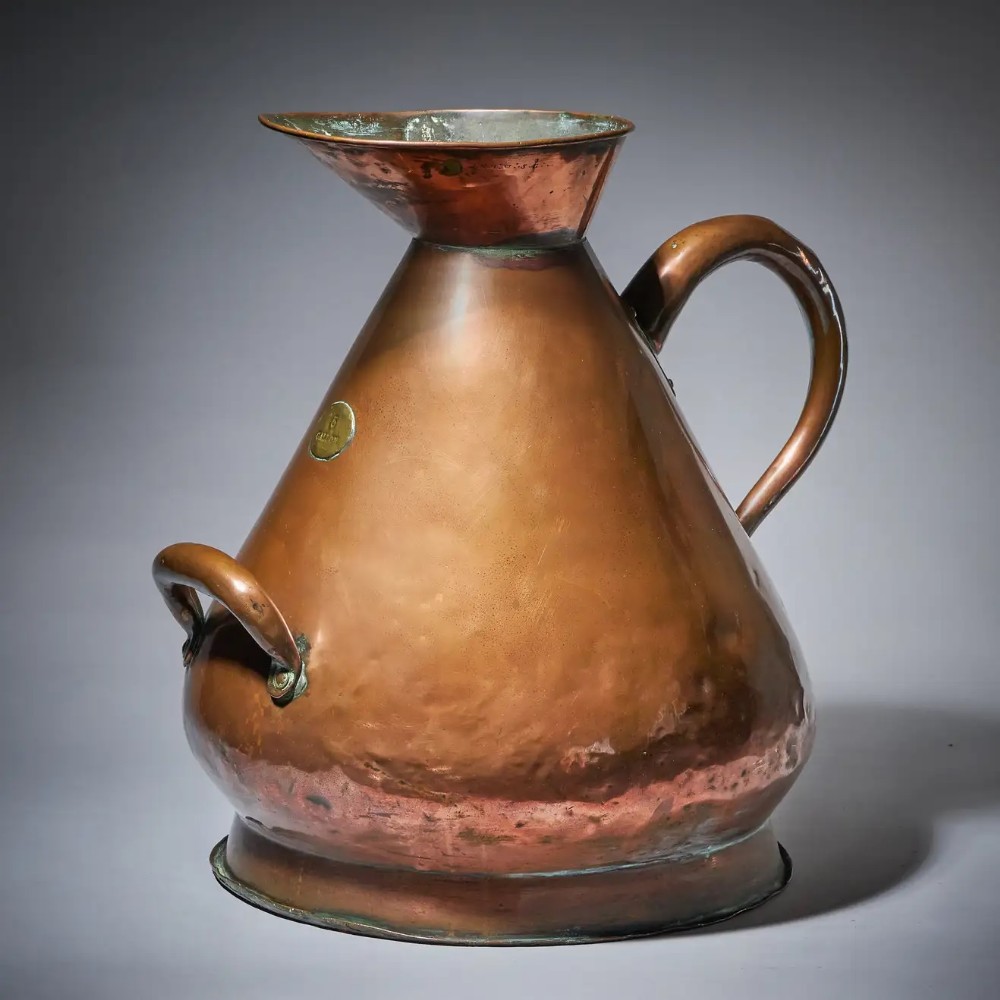 A large conical Victorian hammered copper milk jug with a brass five-gallon capacity badge, dual side handles, and a flared pouring spout.