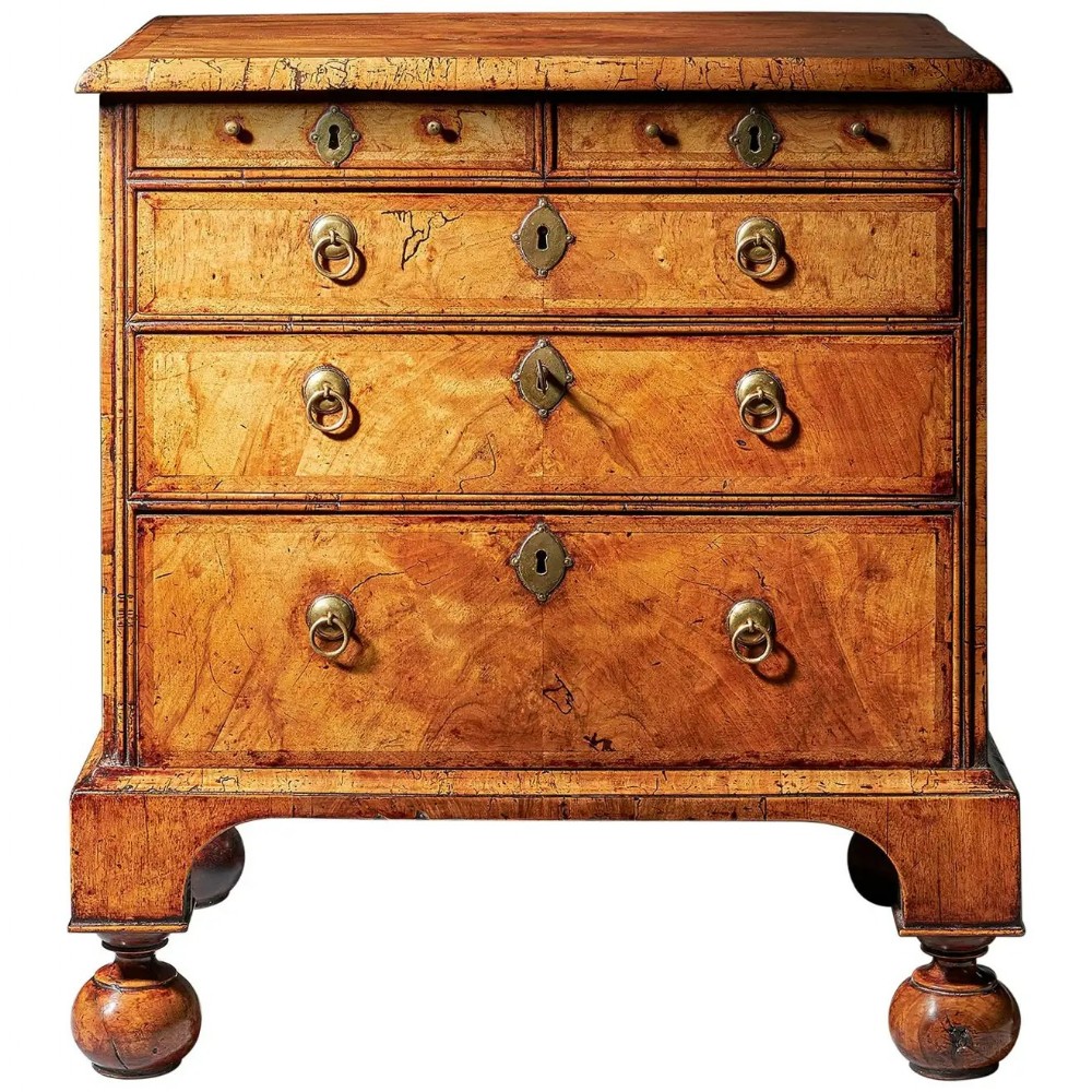 A George I figured walnut chest of drawers featuring brass drop handles, keyhole escutcheons, and a moulded base resting on turned ball and bracket feet.
