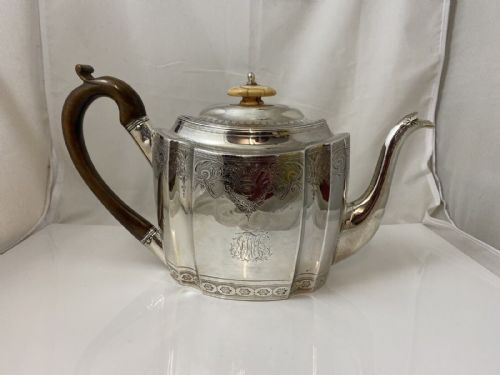 fig 1. An antique silver teapot featuring bright-cut decorative engraving, an engraved central monogram, a carved wooden handle, and a bone lid finial.