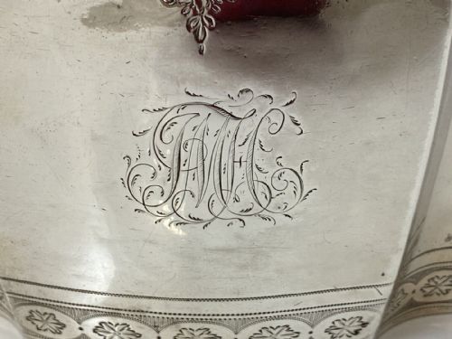 fig 2. An antique silver teapot featuring bright-cut decorative engraving, an engraved central monogram, a carved wooden handle, and a bone lid finial.