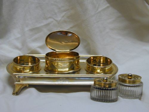 fig 1. A rectangular sterling silver partners inkstand featuring two raised circular inkwells with pierced lids, a central oval box, two pen troughs, and engraved crests.