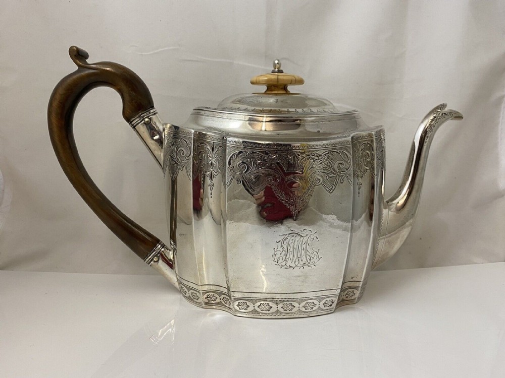 An antique silver teapot featuring bright-cut decorative engraving, an engraved central monogram, a carved wooden handle, and a bone lid finial.