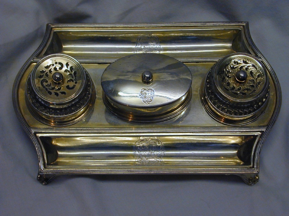 A rectangular sterling silver partners inkstand featuring two raised circular inkwells with pierced lids, a central oval box, two pen troughs, and engraved crests.