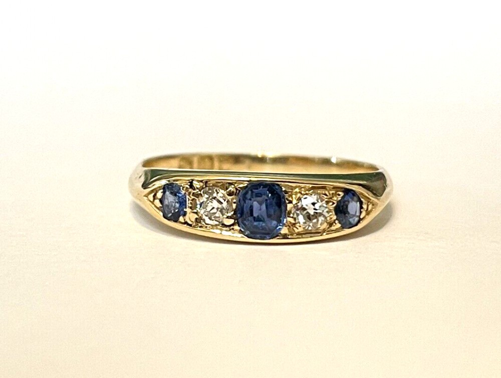 An Edwardian 18ct yellow gold ring set with three blue sapphires alternating with two white diamonds in a carved bridge setting.