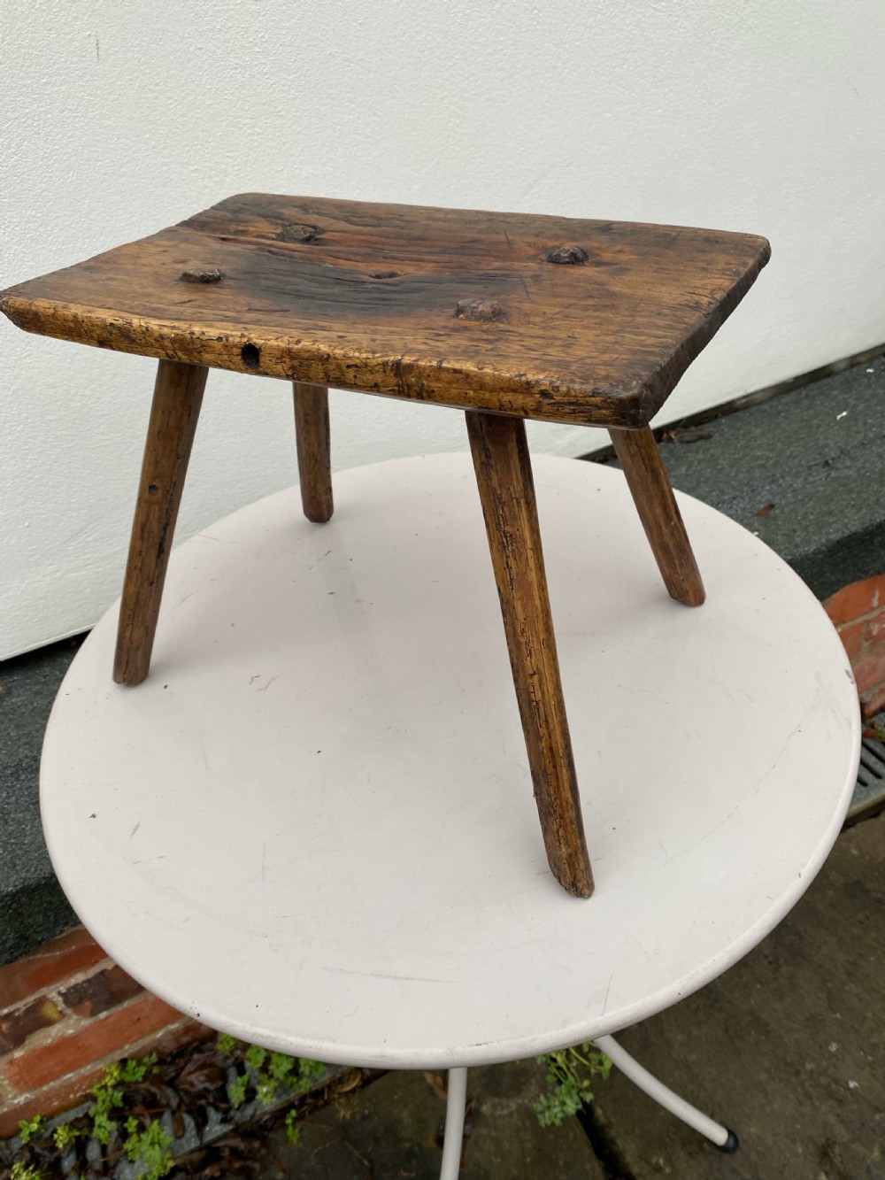 A small primitive wooden rushlight stool featuring four splayed legs wedged through a thick rectangular oak slab top.