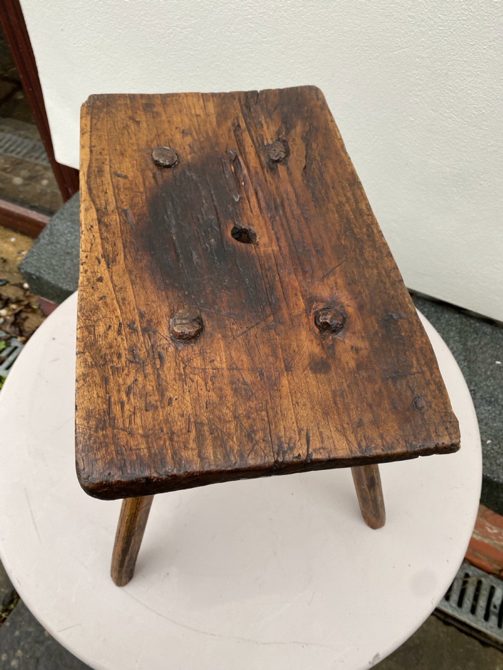 A small primitive wooden rushlight stool featuring four splayed legs wedged through a thick rectangular oak slab top. View II