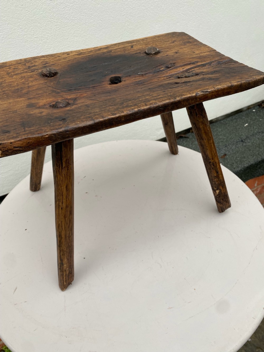 A small primitive wooden rushlight stool featuring four splayed legs wedged through a thick rectangular oak slab top. View IV
