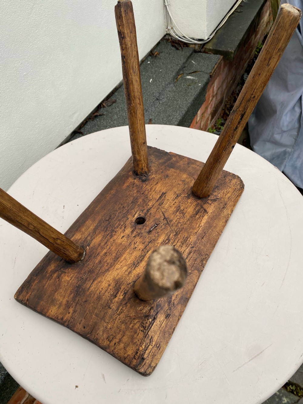 A small primitive wooden rushlight stool featuring four splayed legs wedged through a thick rectangular oak slab top. View V