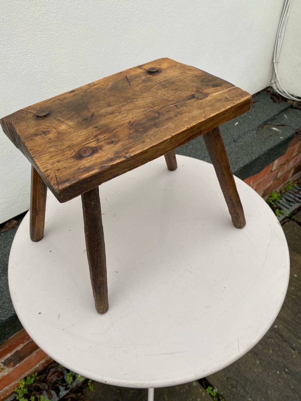 A rustic hand-carved rectangular wooden stool with four tapered legs wedged through a thick solid timber seat.