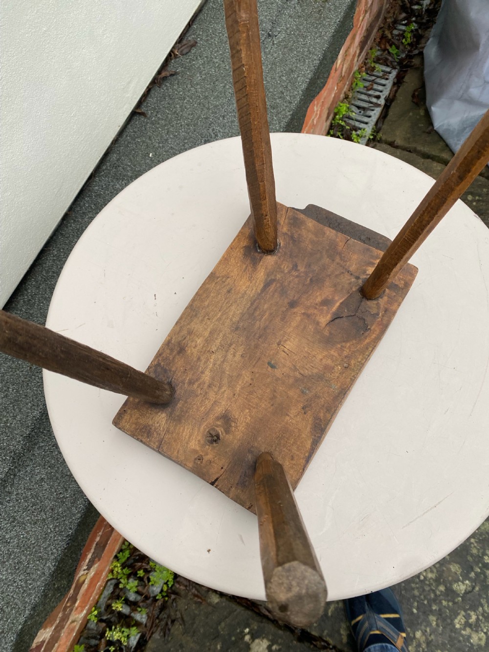 A rustic hand-carved rectangular wooden stool with four tapered legs wedged through a thick solid timber seat. View III