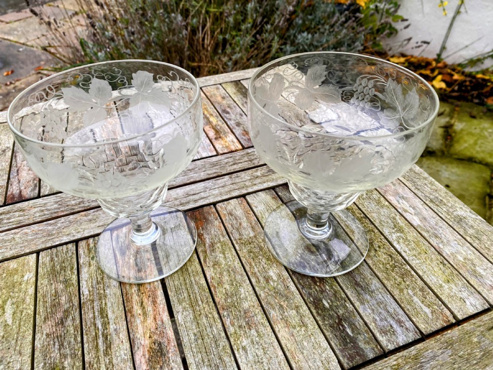 A pair of clear glass rummers decorated with etched grapevine motifs around the wide bowls and short stems.