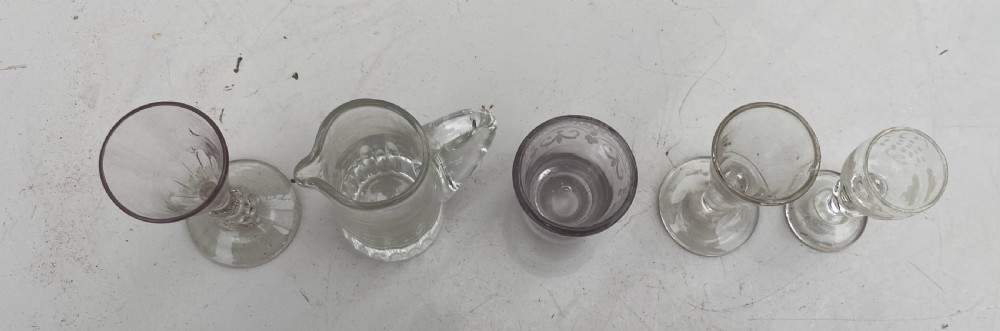 A set of five miniature glass vessels including stemmed cordial glasses, an etched tumbler, and a small jug lined up on a white surface. View III