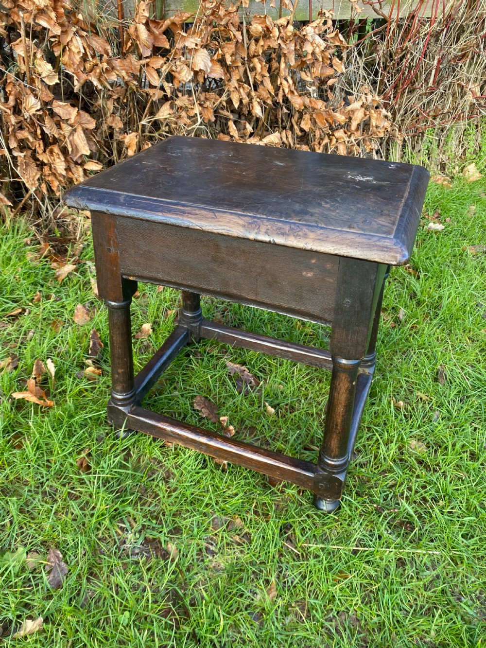 A dark oak joint stool featuring a rectangular top, rectangular frame apron, four turned legs, and low perimeter stretchers.