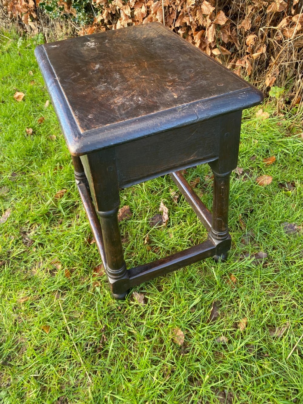 A dark oak joint stool featuring a rectangular top, rectangular frame apron, four turned legs, and low perimeter stretchers. View V