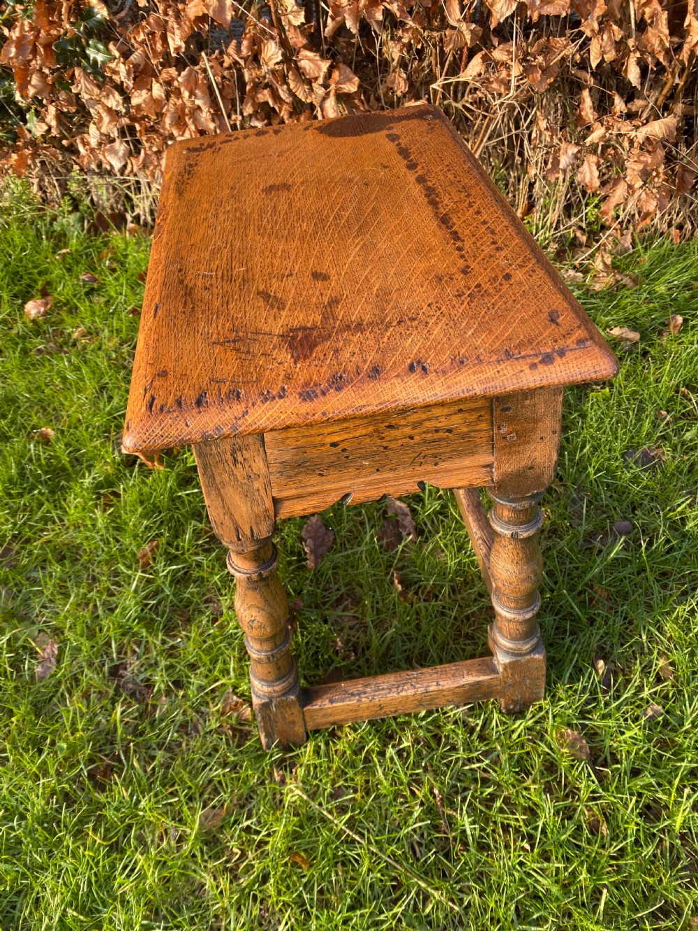A solid oak joint stool featuring turned legs, lower perimeter stretchers, a shaped frieze apron, and a rectangular seat top. View III