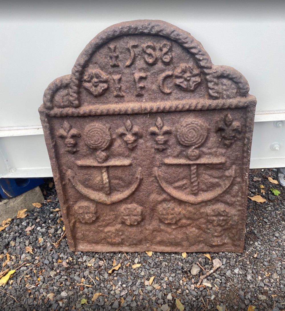 An arched Elizabethan cast iron fireback featuring the date 1588, initials, rope moulding, and embossed anchor and fleur-de-lis motifs.
