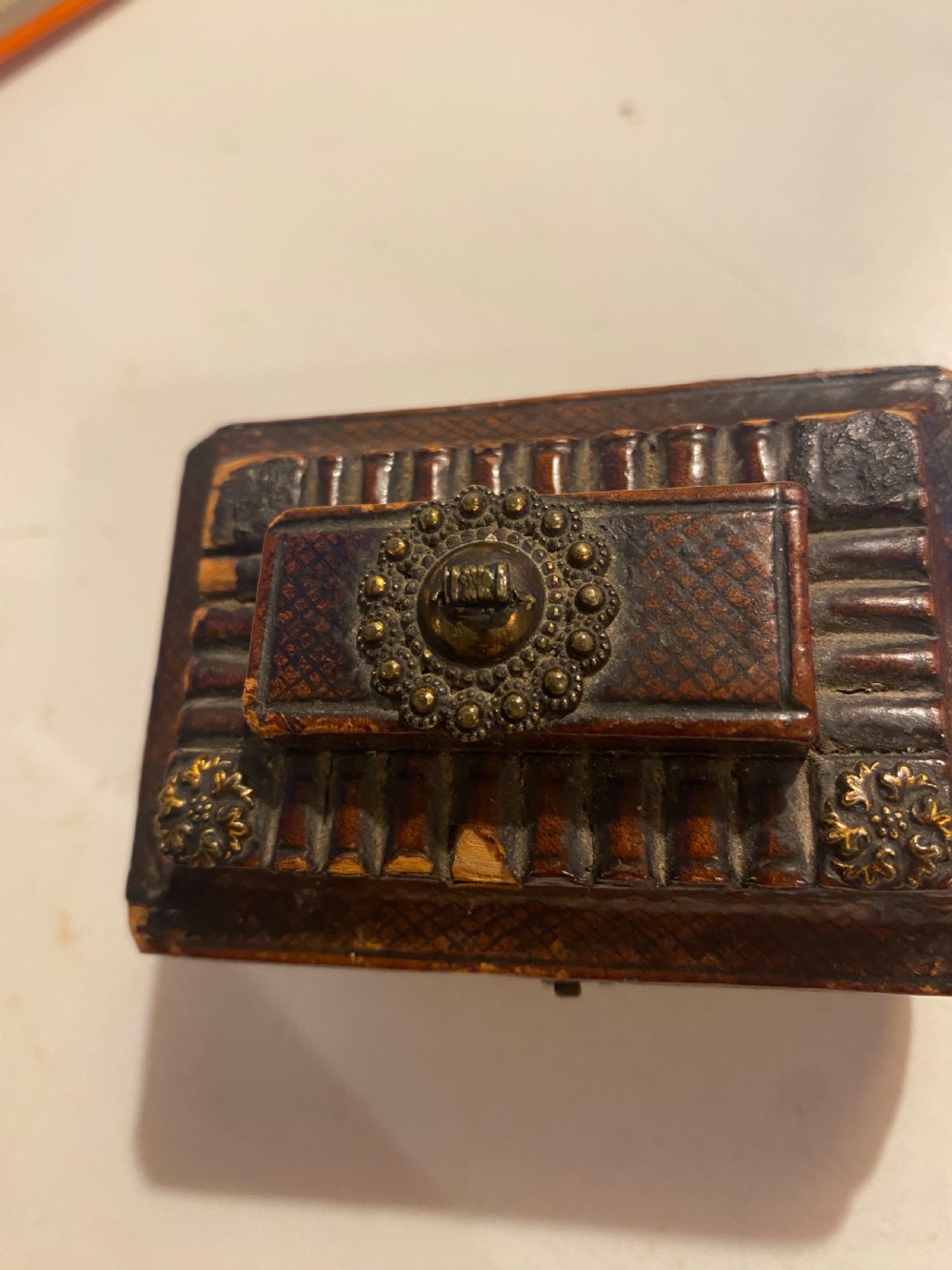 An antique dark brown tooled leather trinket box featuring a tiered lid with decorative brass mounts, brass hook clasp, and round ball feet. View XII