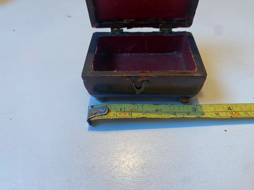 An antique dark brown tooled leather trinket box featuring a tiered lid with decorative brass mounts, brass hook clasp, and round ball feet. View XIII