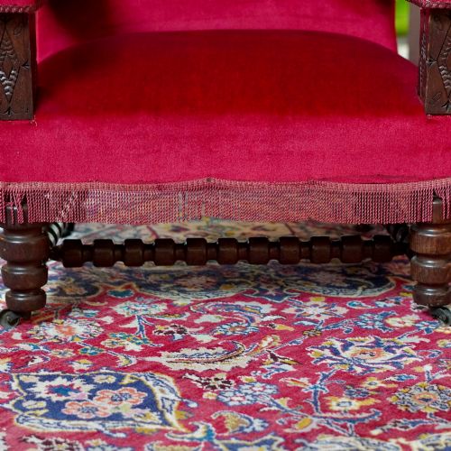 fig 7. A pair of oversized Victorian armchairs upholstered in crimson red velvet with fringe trim, featuring carved oak arm supports and bobbin-turned legs.