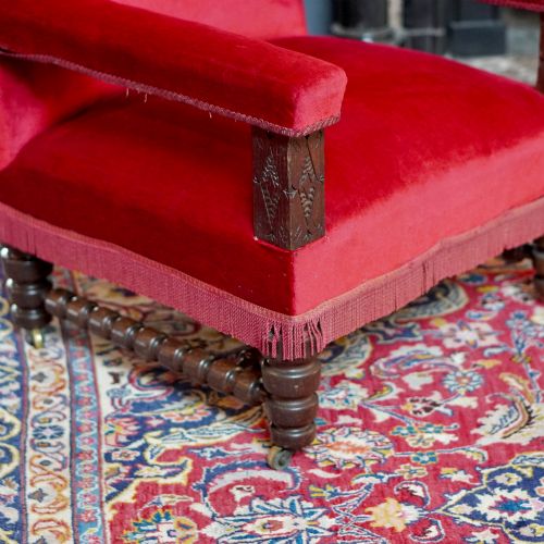 fig 8. A pair of oversized Victorian armchairs upholstered in crimson red velvet with fringe trim, featuring carved oak arm supports and bobbin-turned legs.