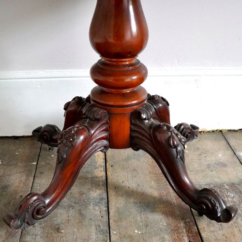 fig 6. A Victorian figured mahogany card table featuring a turnover top, carved frieze, turned pedestal, and scroll legs with castors.