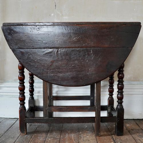 fig 2. A dark brown antique oak gateleg drop-leaf table with turned legs and an oval top.