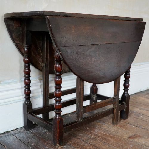 fig 3. A dark brown antique oak gateleg drop-leaf table with turned legs and an oval top.