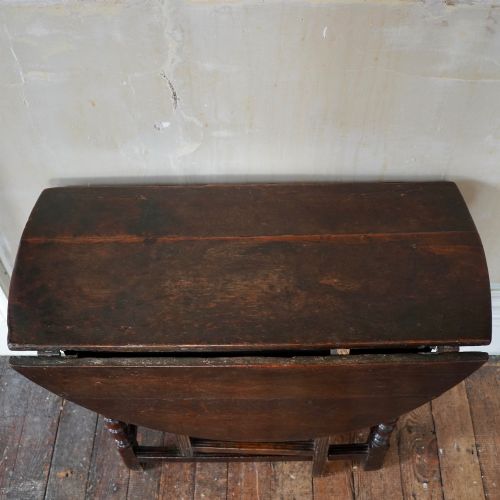 fig 4. A dark brown antique oak gateleg drop-leaf table with turned legs and an oval top.