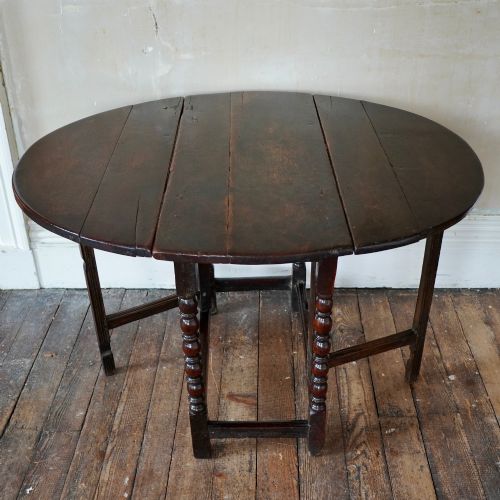 fig 5. A dark brown antique oak gateleg drop-leaf table with turned legs and an oval top.