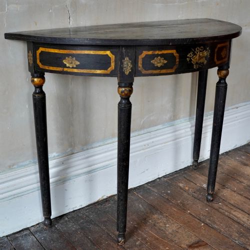 fig 1. A Regency period semi-circular console table painted black with gold-gilded classical panel motifs and four slender turned legs.