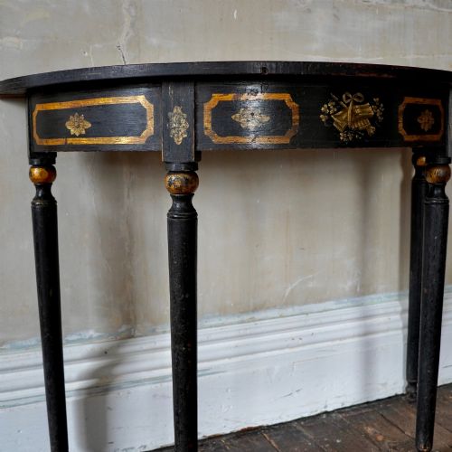 fig 4. A Regency period semi-circular console table painted black with gold-gilded classical panel motifs and four slender turned legs.