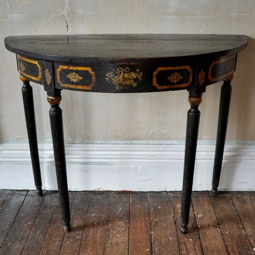 fig 5. A Regency period semi-circular console table painted black with gold-gilded classical panel motifs and four slender turned legs.