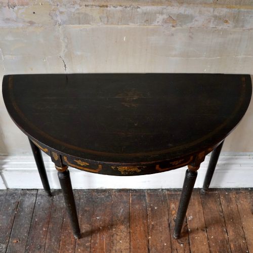fig 7. A Regency period semi-circular console table painted black with gold-gilded classical panel motifs and four slender turned legs.