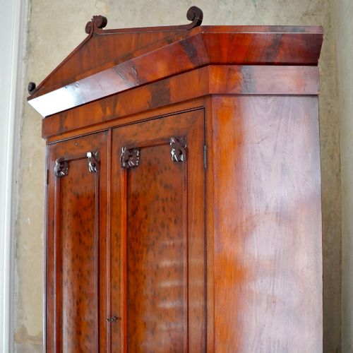 fig 5. A tall, two-tier William IV corner cupboard crafted from dark plum pudding mahogany, featuring panelled double doors on both top and bottom sections with carved detail and a pediment top.