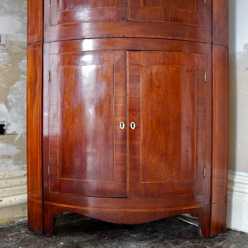 fig 2. A tall Georgian mahogany bowfront corner cupboard featuring two upper curved doors, two lower curved doors, and fine line inlay.
